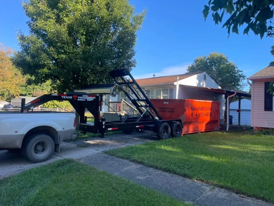 Kelley Roll Offs truck and trailer delivering an orange dumpster